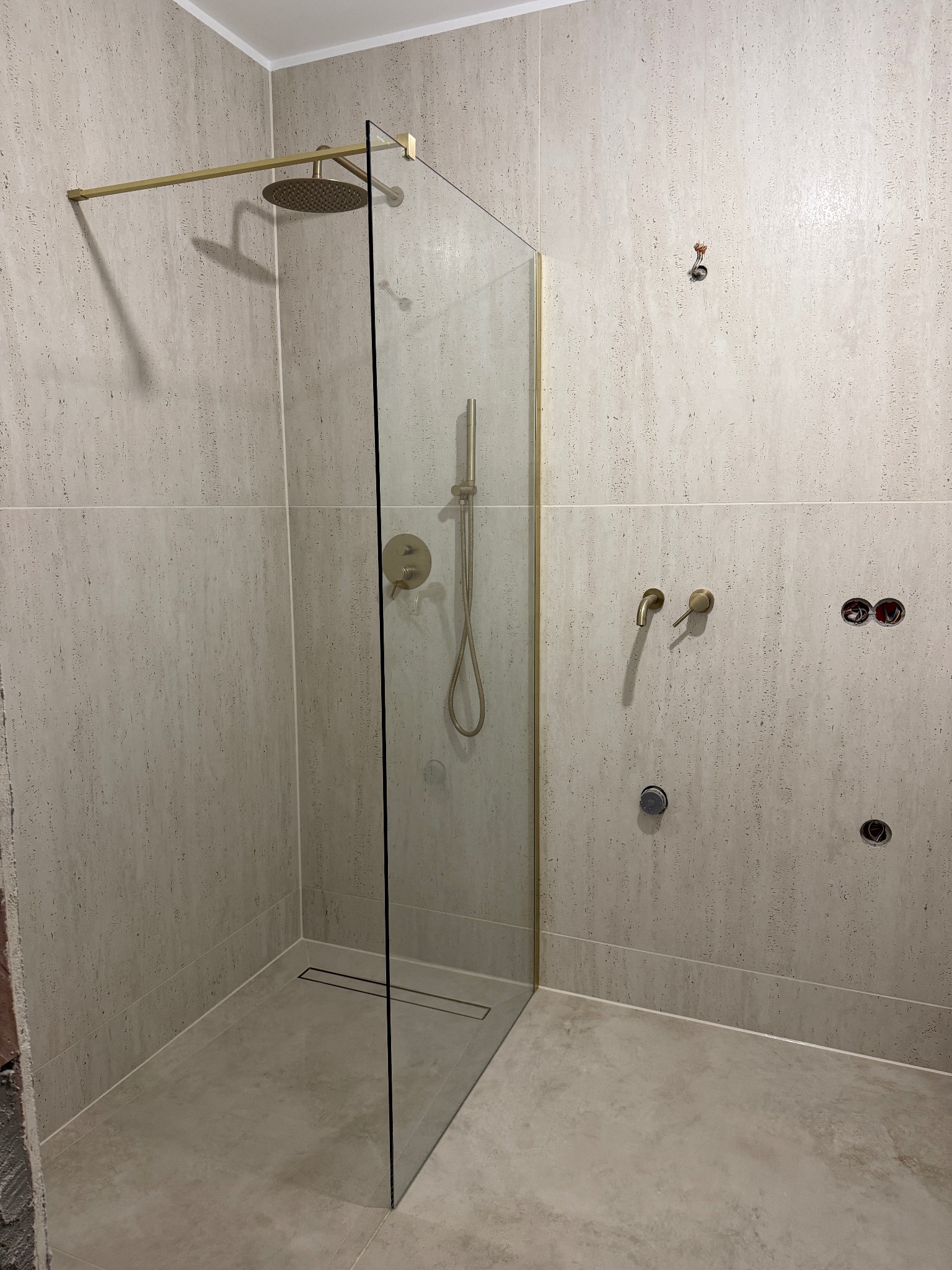 Wykończona kabina prysznicowa typu walk-in z elementami w kolorze złotym, widoczne płytki na ścianach i podłodze oraz przygotowane punkty instalacyjne.