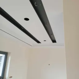 Nowoczesny sufit podwieszany z czarnymi elementami dekoracyjnymi i otworami na oświetlenie w jasnym wnętrzu w trakcie montażu.