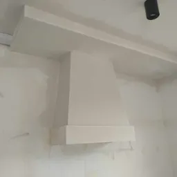 Konstrukcja z płyt gipsowo-kartonowych zabudowująca okap kuchenny, świeżo pomalowana na biało, widoczne niedoskonałości na ścianie i przewodach elektrycznych.