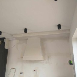 Sylwester Piotrowski - Wnętrze kuchni w trakcie prac wykończeniowych: ściany po szpachlowaniu, przygotowane do malowania, widoczne czarne lampy sufitowe, biały okap i poziomica laserowa.