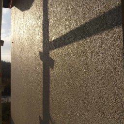 Sylwester Piotrowski - Świeżo nałożona, błyszcząca faktura na elewacji budynku w słoneczny dzień, widoczny cień rusztowania.