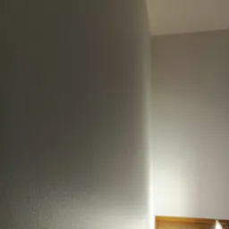 Szara ściana wewnętrzna z widoczną fakturą, oświetlona od dołu, z drewnianą podłogą w tle.