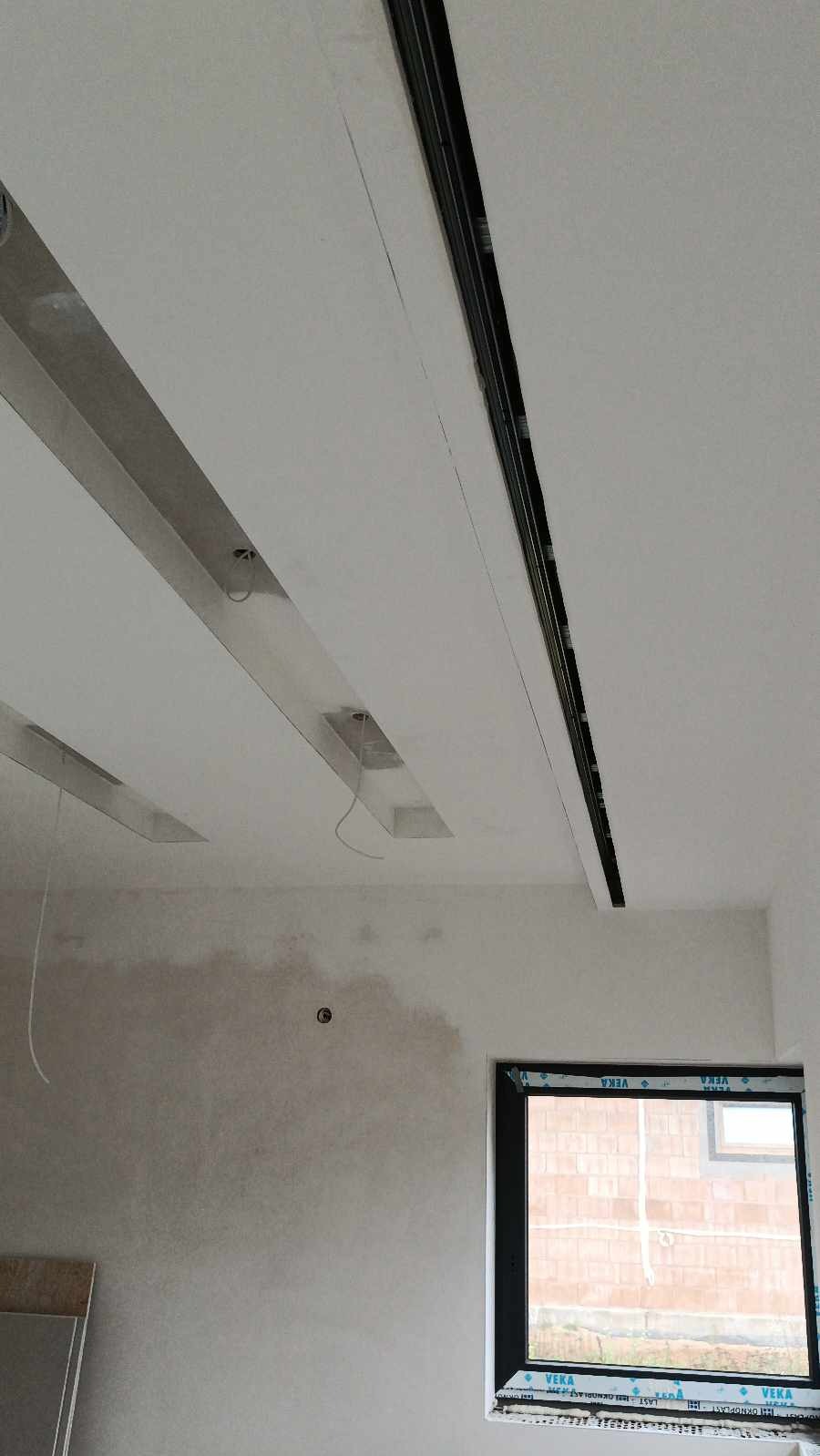 Montaż sufitu z elementami podświetlenia LED w nowym budownictwie; widoczne niedoskonałości na ścianie przed malowaniem.