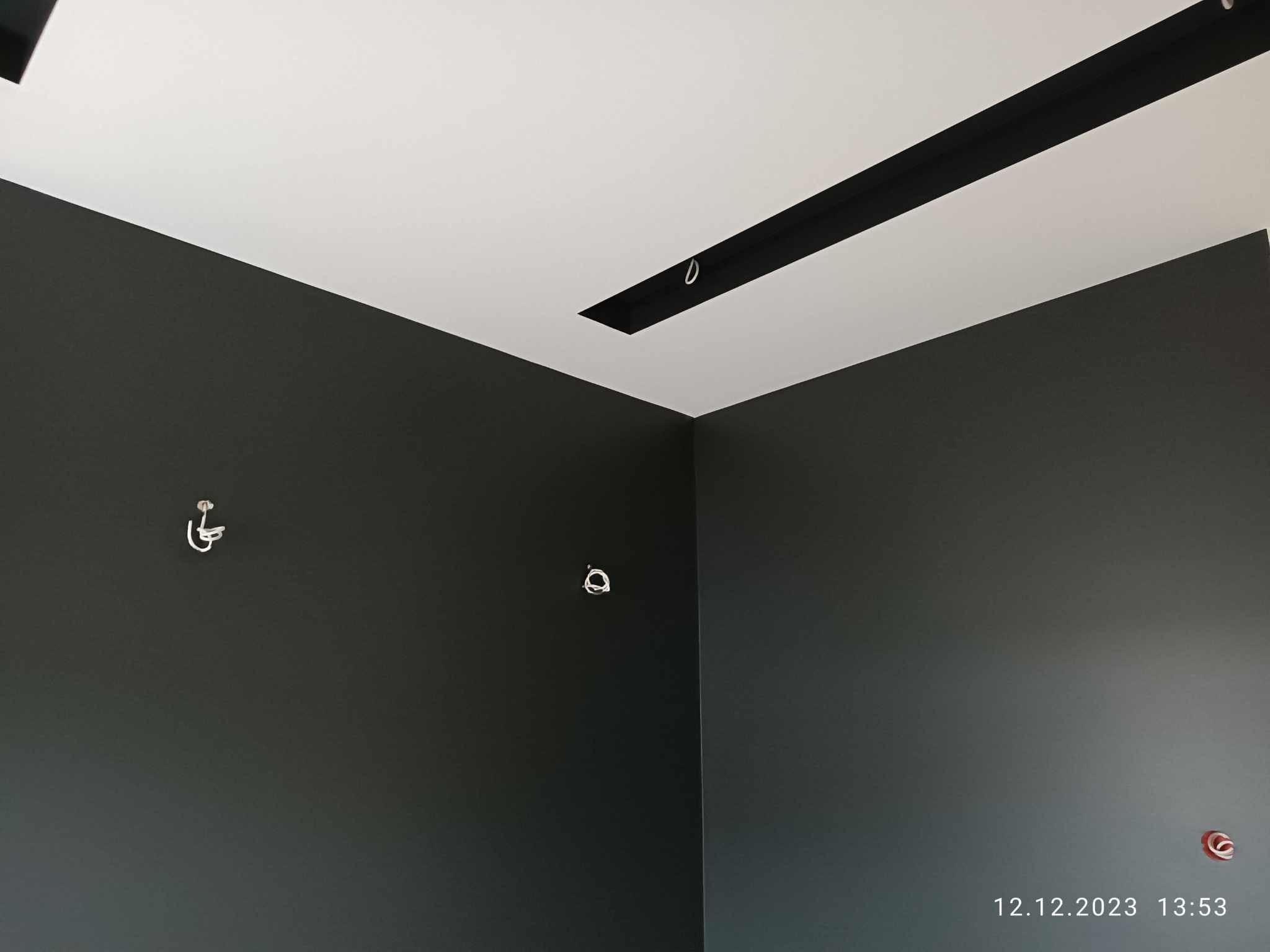 Pomieszczenie po remoncie: ciemnoszare ściany z widocznymi punktami instalacji elektrycznej oraz biały sufit z czarną listwą oświetleniową.