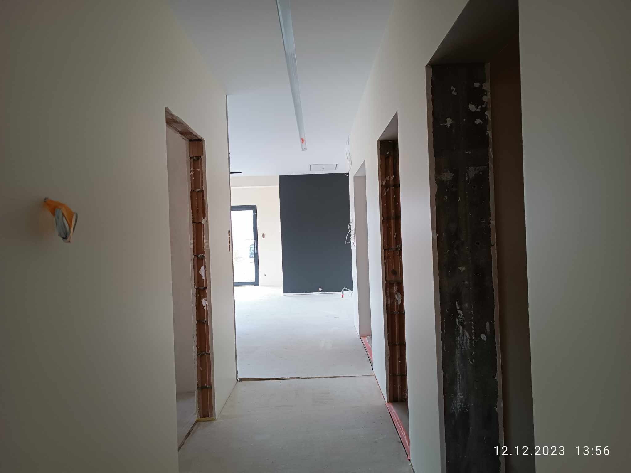 Korytarz w trakcie prac wykończeniowych, ściany po nałożeniu gładzi i wstępnym malowaniu, widoczne surowe ościeżnice drzwiowe i przygotowane podłoże pod posadzkę.