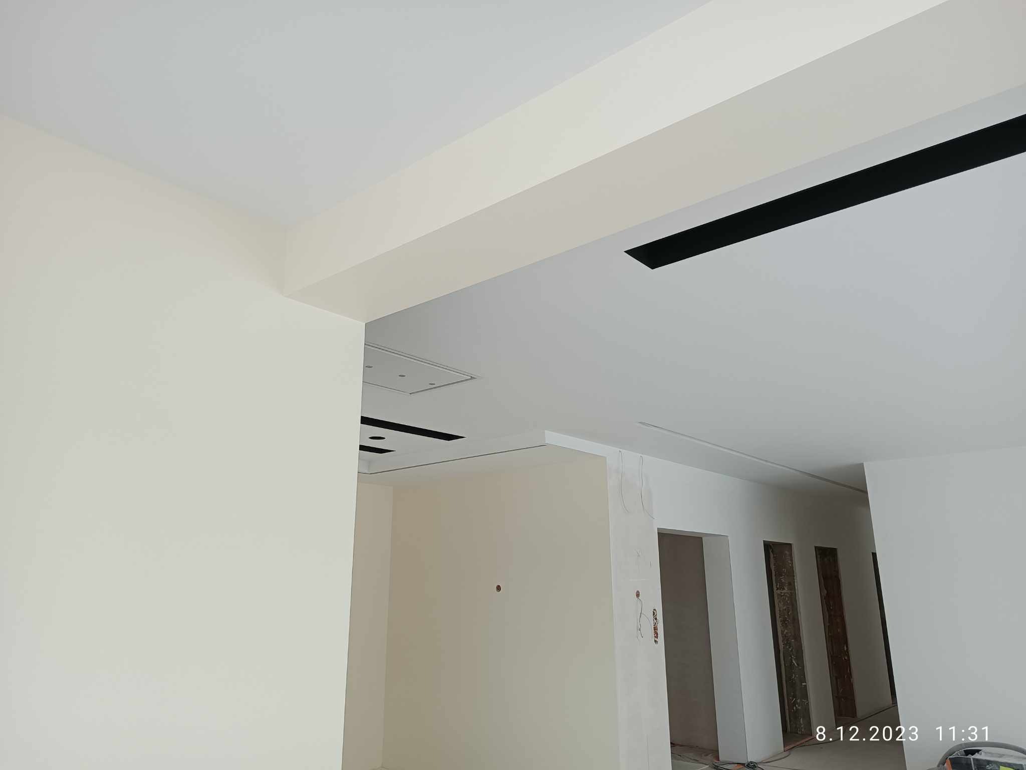 Wnętrze w trakcie prac wykończeniowych: świeżo pomalowane ściany w odcieniach bieli, widoczne elementy sufitu podwieszanego z czarnymi akcentami, przygotowane otwory drzwiowe.