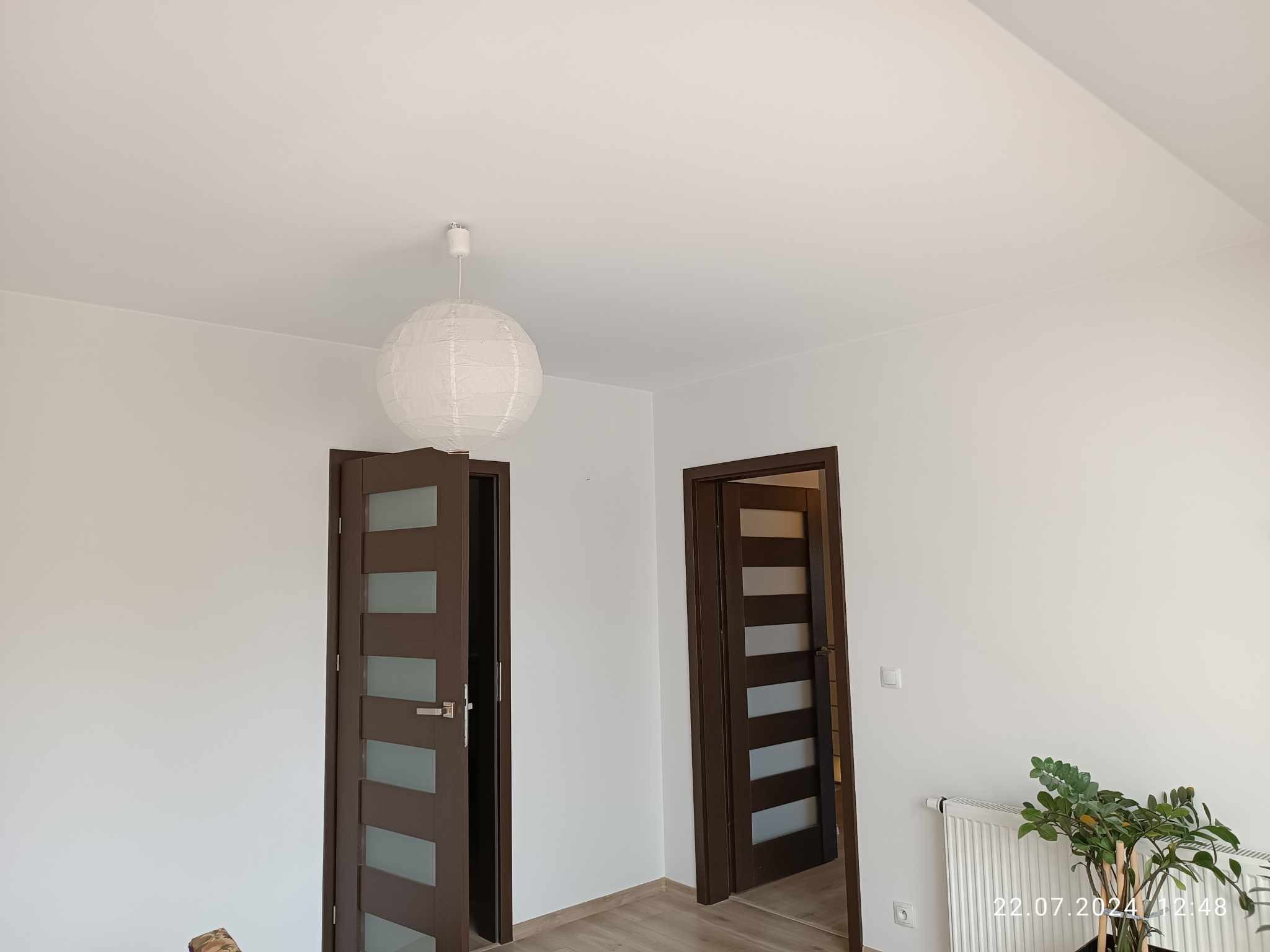 Wnętrze pokoju po remoncie z dwoma otwartymi, nowoczesnymi drzwiami z przeszkleniami, świeżo pomalowanymi ścianami na biało i okrągłą lampą wiszącą.