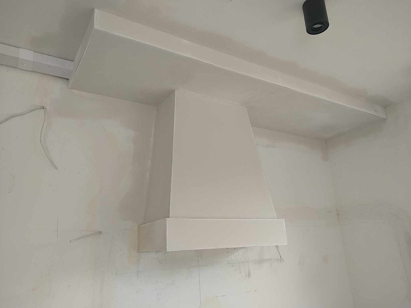 Konstrukcja z płyt gipsowo-kartonowych zabudowująca okap kuchenny, świeżo pomalowana na biało, widoczne niedoskonałości na ścianie i przewodach elektrycznych.