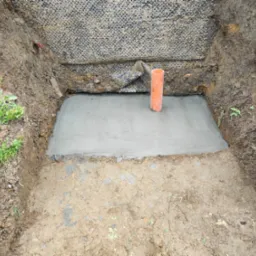 Wybetonowany fundament z wystającą rurą kanalizacyjną, zabezpieczony od strony gruntu czarną folią drenażową.