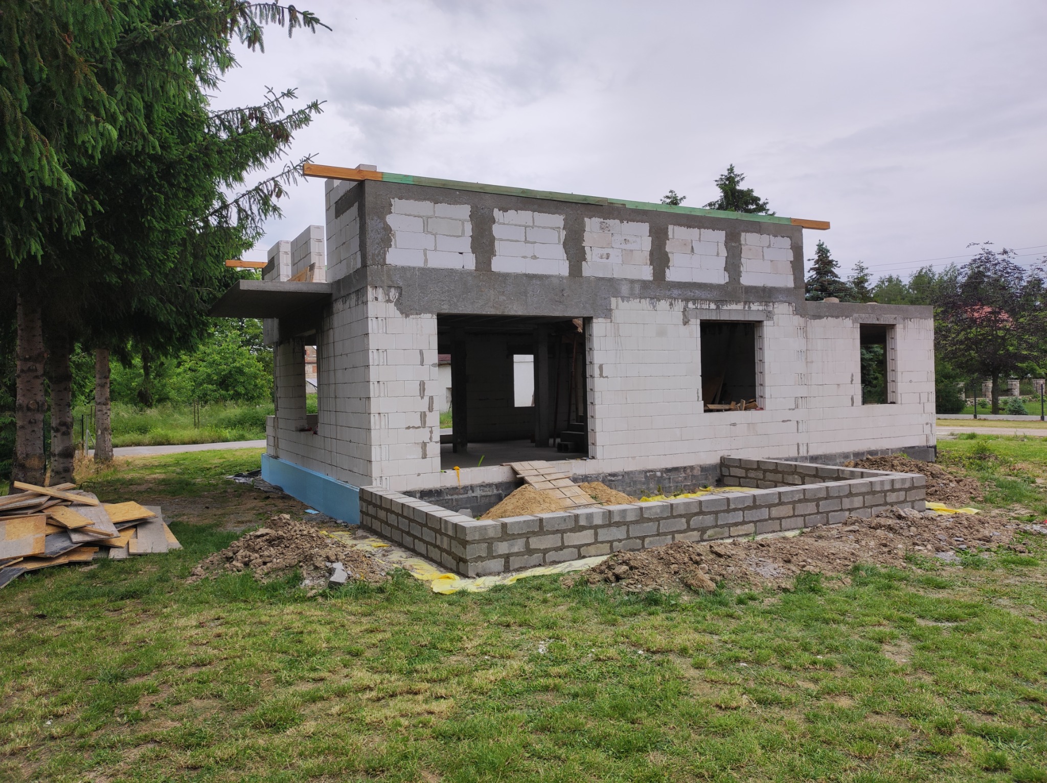 Wznoszenie ścian z betonu komórkowego Ytong na budowie domu jednorodzinnego, widoczna izolacja fundamentów i tymczasowe drewniane podpory stropu.