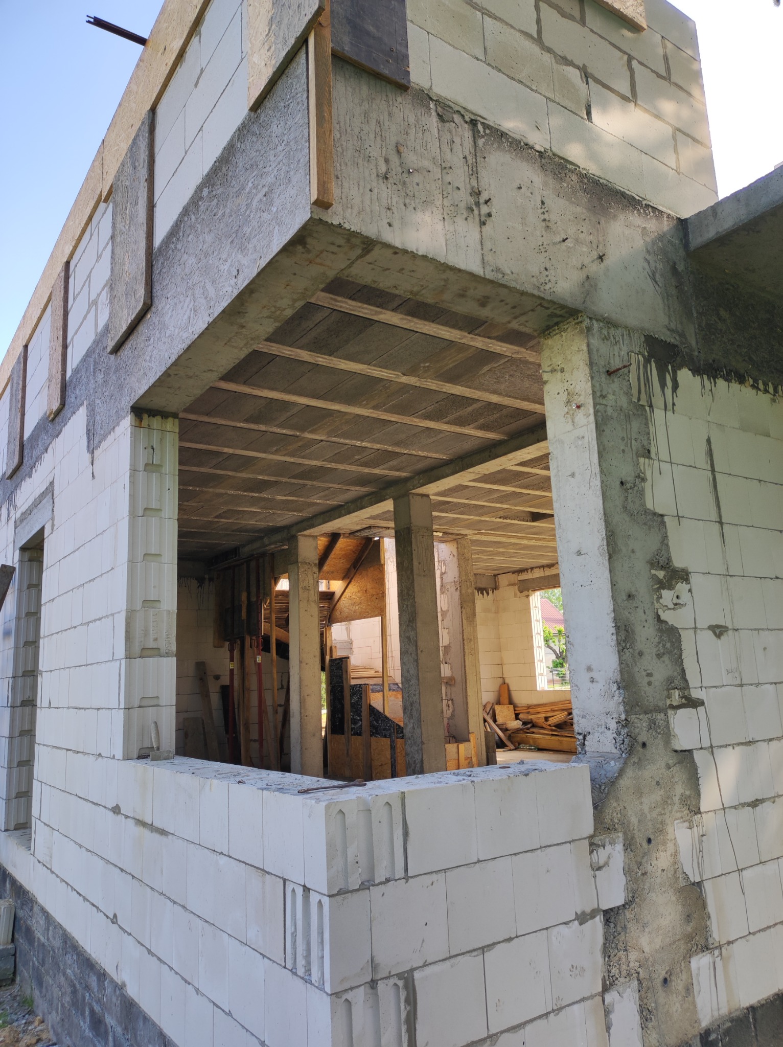 Surowy stan domu w trakcie budowy, widoczne ściany z bloczków, betonowy strop i słupy, drewniane elementy szalunków.