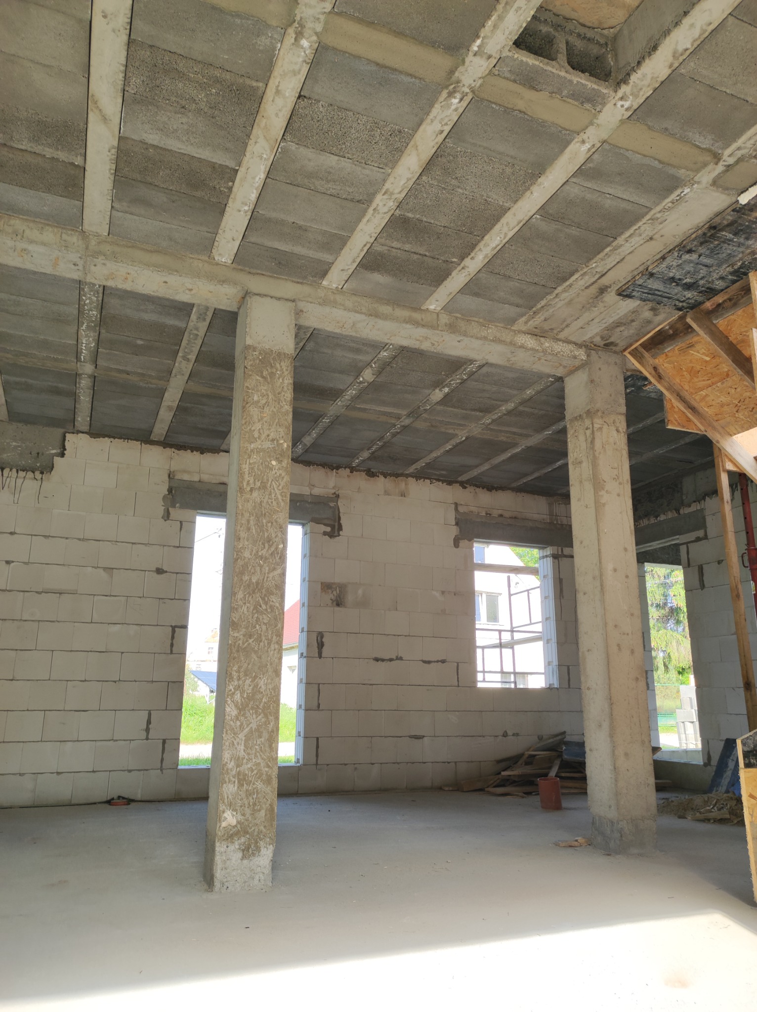 Wnętrze surowego domu w Ostroszowicach, widoczne ściany z białych bloczków, betonowy strop z żebrami i słupami, otwory okienne bez ram.