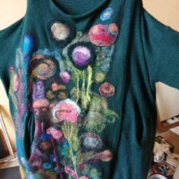 Zielona tunika damska z ręcznie haftowanymi, abstrakcyjnymi kwiatami w odcieniach różu, fioletu i błękitu, widoczne kieszenie i luźny krój.