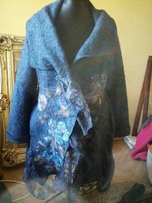 Niebieska, filcowa kurtka damska z motywami kwiatowymi i koronkowymi aplikacjami, prezentowana na manekinie, z widoczną złotą ramą lustra w tle.