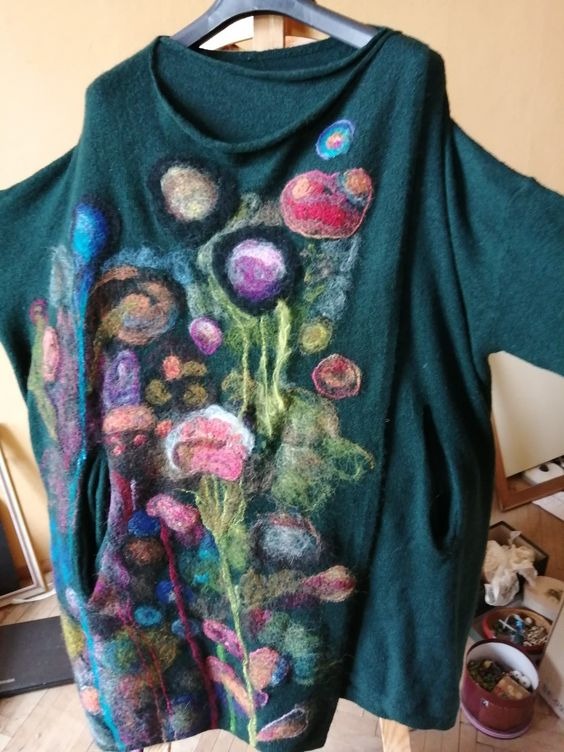 Zielona tunika damska z ręcznie haftowanymi, abstrakcyjnymi kwiatami w odcieniach różu, fioletu i błękitu, widoczne kieszenie i luźny krój.