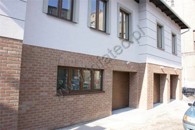 Elewacja budynku z zastosowanym systemem dociepleń z klinkierem INFATEC, widoczne okna z brązowymi ramami i fragment niebieskiego samochodu.