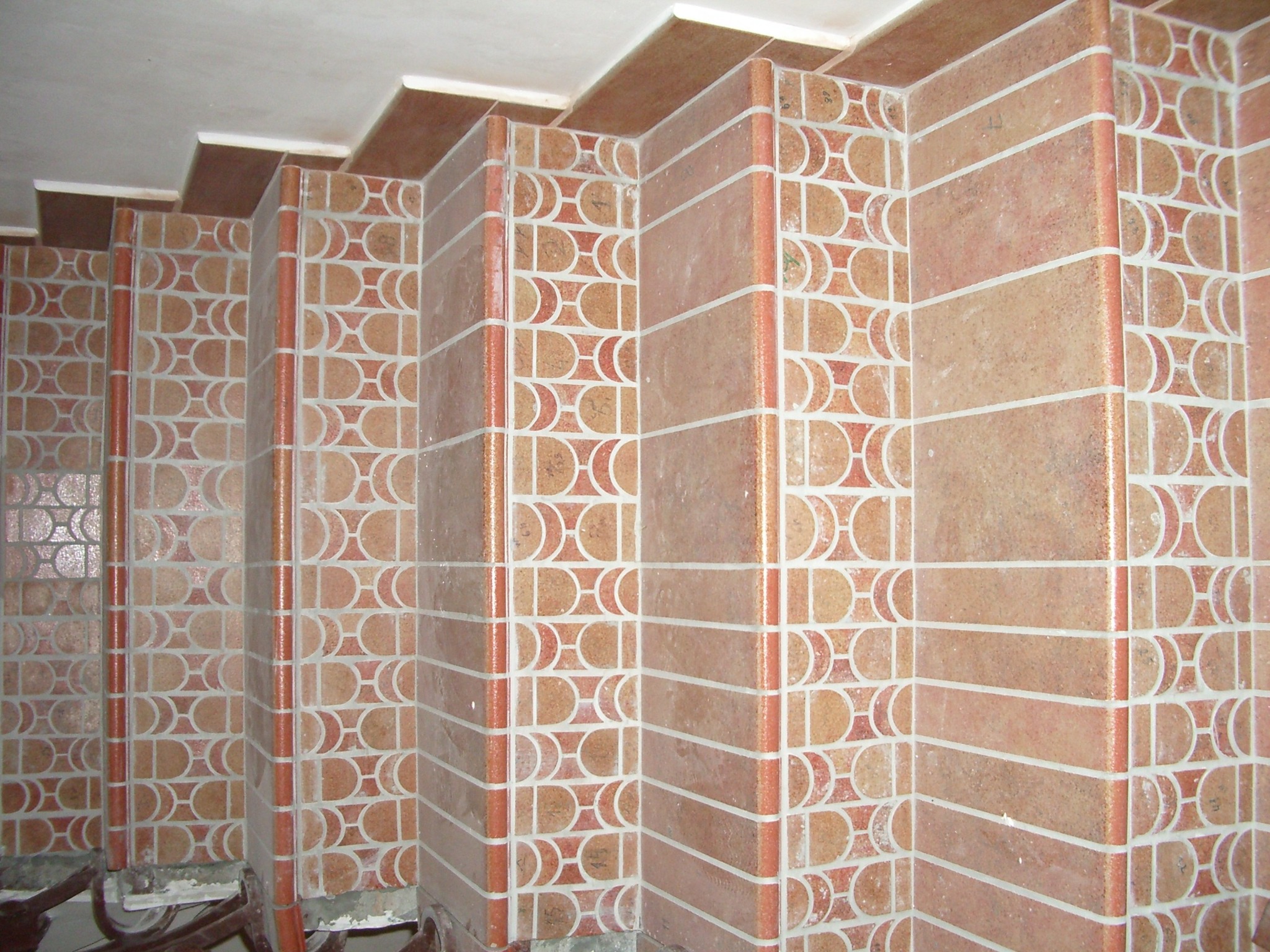 Wykończone kafelkami schody wewnętrzne o geometrycznym wzorze w odcieniach brązu i beżu, widok z góry, częściowo widoczne metalowe elementy konstrukcyjne.