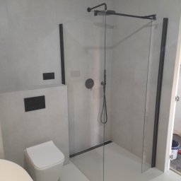 Mid-Ar Wykończenia Wnętrz - Nowoczesna łazienka z kabiną prysznicową typu walk-in z czarnymi profilami, podwieszaną toaletą i szarą glazurą.