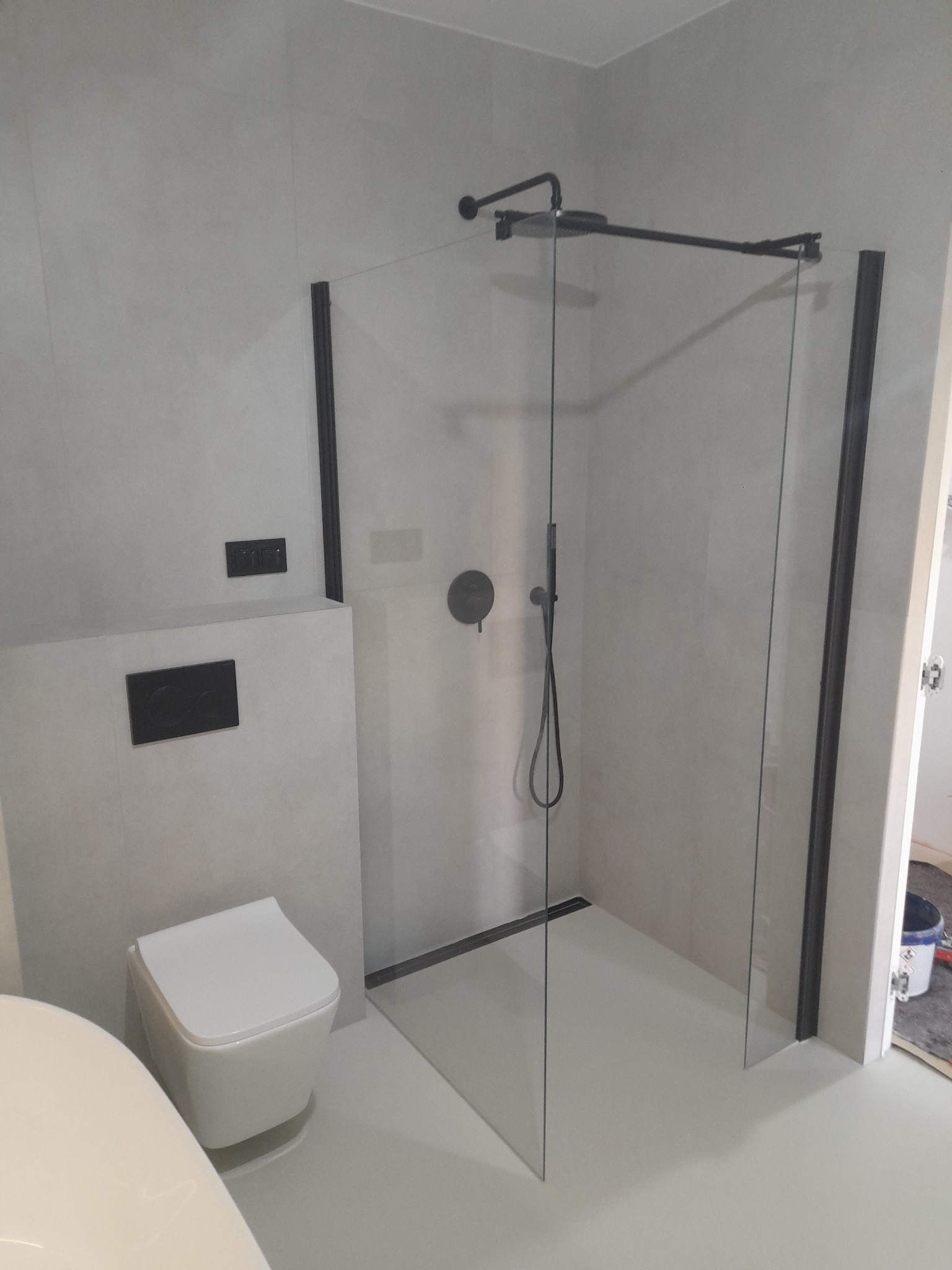 Nowoczesna łazienka z kabiną prysznicową typu walk-in z czarnymi profilami, podwieszaną toaletą i szarą glazurą.