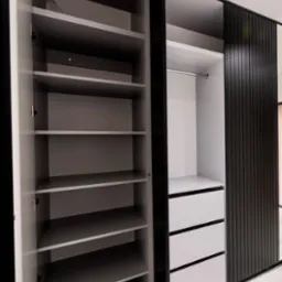 Otwarta szafa z półkami i szufladami, czarne pionowe panele na drzwiach przesuwnych, widok z bliska na wnętrze szafy.