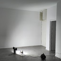 D&K Oleksandr Kruhliak - Przygotowane do malowania pomieszczenie z białymi ścianami, szarą podłogą i trzema lampami halogenowymi oświetlającymi ściany.