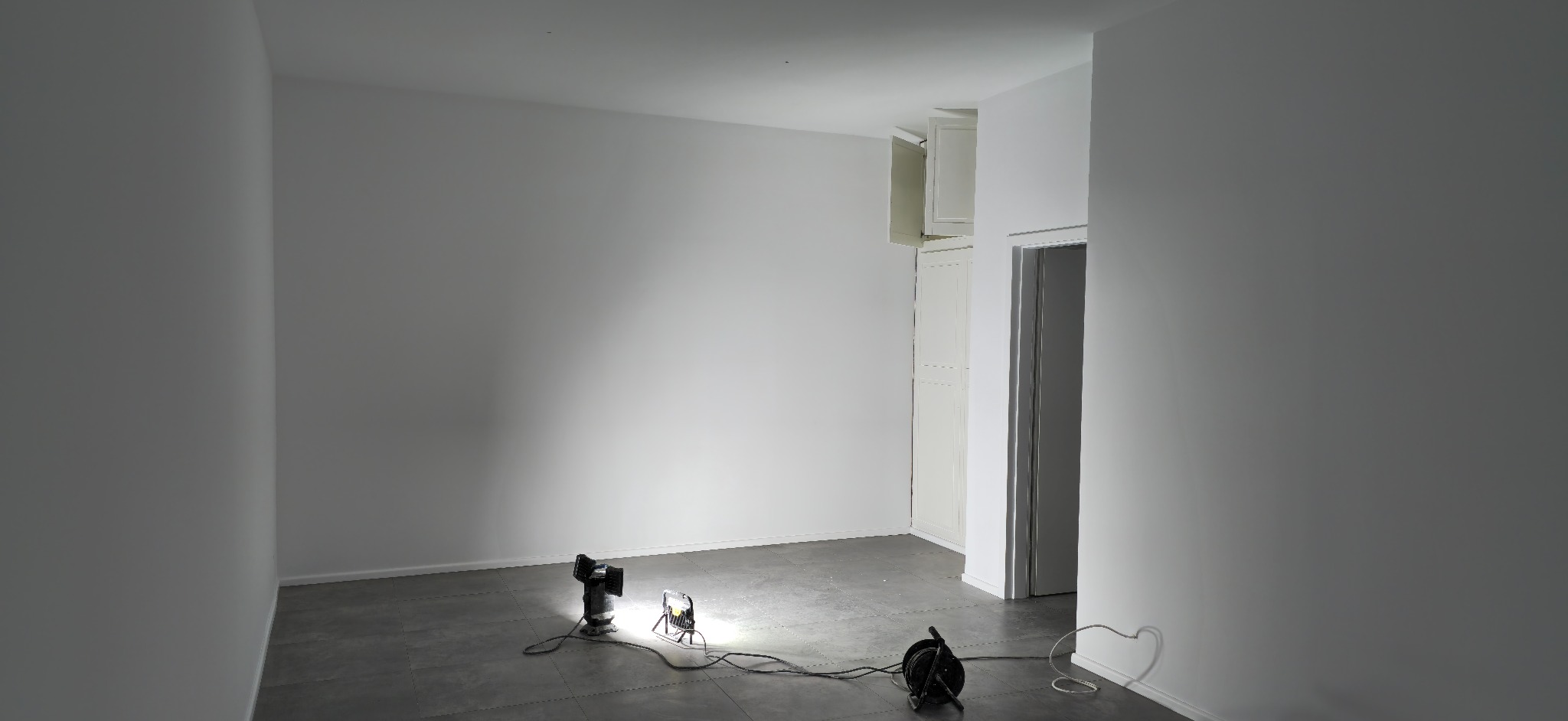 Przygotowane do malowania pomieszczenie z białymi ścianami, szarą podłogą i trzema lampami halogenowymi oświetlającymi ściany.