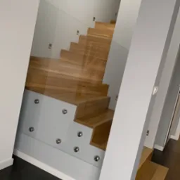 Nowoczesne schody drewniane z przeszkloną balustradą, mocowaną za pomocą metalowych punktowych uchwytów, w jasnym wnętrzu z ciemną podłogą.