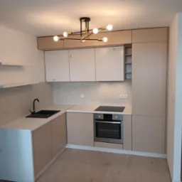 Jasna kuchnia z beżowymi frontami i białymi szafkami g&oacute;rnymi z ryflowanym wzorem, czarny zlew i bateria, nowoczesna lampa sufitowa z kulistymi kloszami.