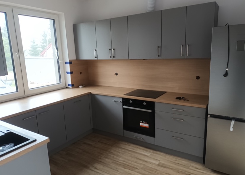 Szare meble kuchenne na wymiar z drewnianym blatem i oświetleniem podszafkowym, widok na okno z taśmą malarską.