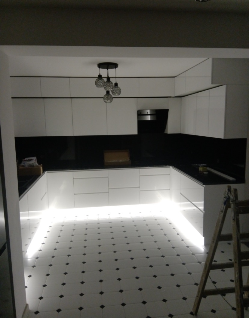 Nowoczesna, biała kuchnia z czarnym blatem i podświetleniem LED w Krakowie, widoczna drabina malarska.