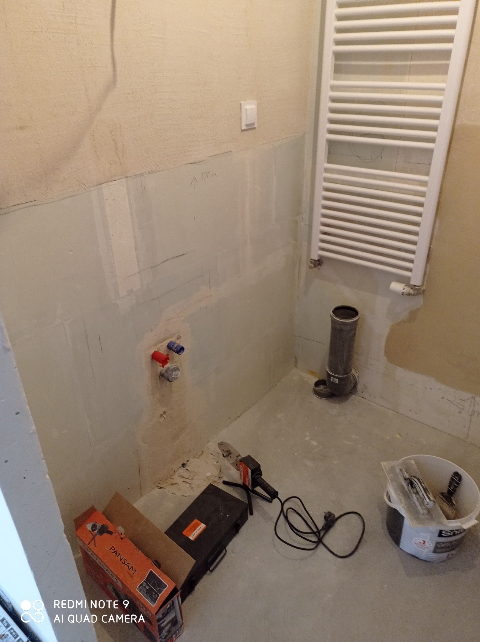 Łazienka w trakcie remontu: ściany przygotowane do położenia płytek, widoczne rury, grzejnik drabinkowy, narzędzia i materiały budowlane.