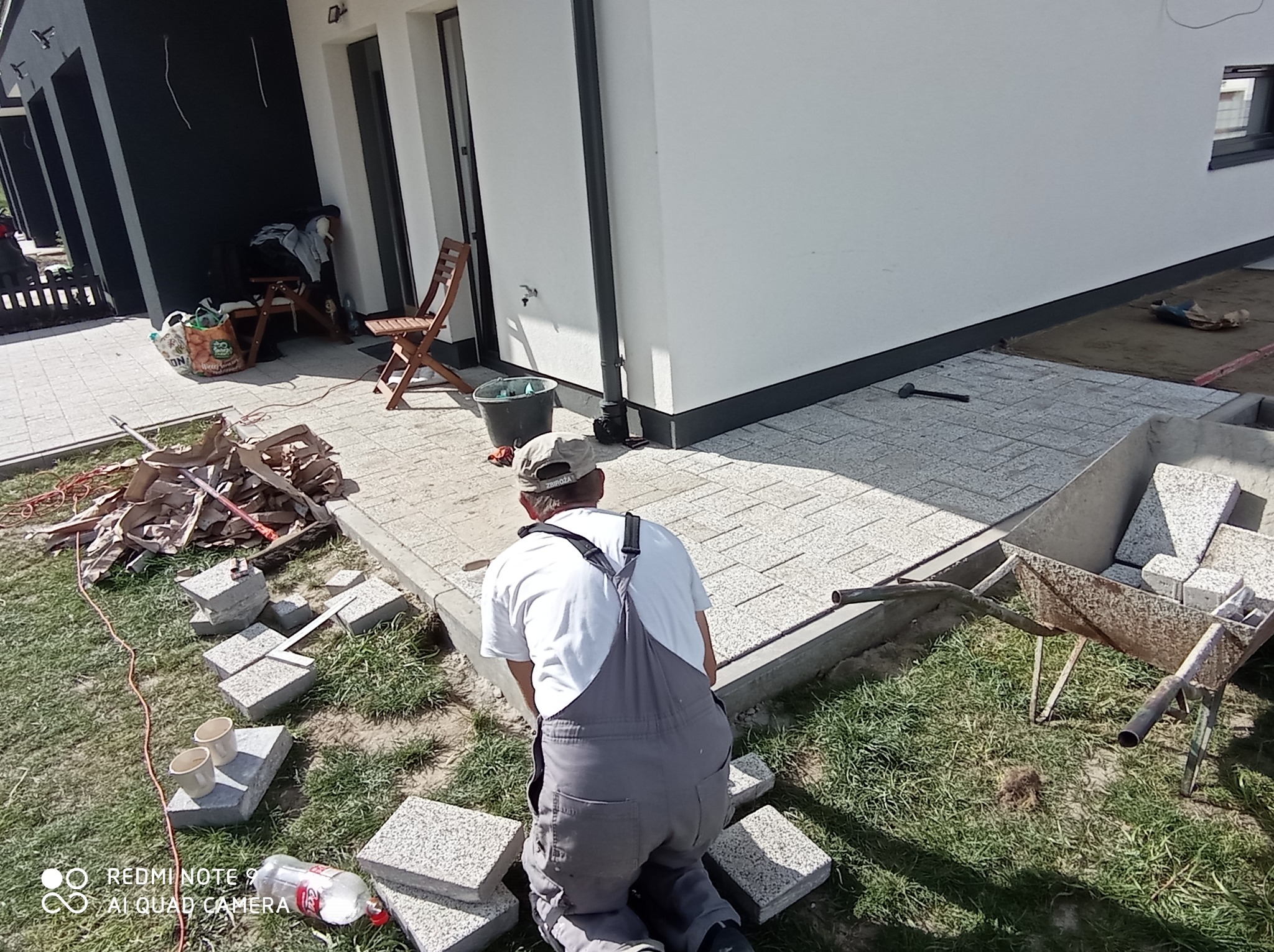 Pracownik w trakcie układania jasnoszarej kostki brukowej na posesji domu jednorodzinnego. Widoczny fragment ułożonej nawierzchni i przygotowane materiały.