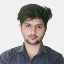 Portret młodego mężczyzny z ciemnymi włosami i lekkim zarostem, ubranego w ciemną koszulę na jednolitym, jasnym tle.