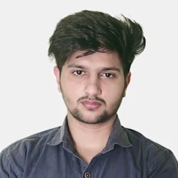 Portret młodego mężczyzny z ciemnymi włosami i lekkim zarostem, ubranego w ciemną koszulę na jednolitym, jasnym tle.