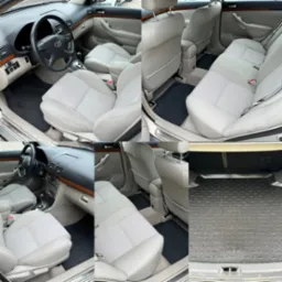 Wnętrze samochodu Toyota Avensis: jasnoszare tapicerki foteli i podłokietników, czarne gumowe dywaniki, deska rozdzielcza z elementami drewnopodobnymi, bagażnik z gumową wykładziną z napisem Avensis.