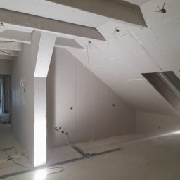 REMONTY DAMIAN DUSZCZAK - Poddasze w trakcie wykańczania płytami kartonowo-gipsowymi, widoczne stelaże, instalacje elektryczne i okno dachowe, stan surowy przed malowaniem.