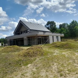 REMONTY DAMIAN DUSZCZAK - Nowoczesny dom jednorodzinny w trakcie wykończenia elewacji, widoczne rusztowania i szara kolorystyka budynku na tle błękitnego nieba z chmurami.