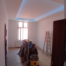 REMONTY DAMIAN DUSZCZAK - Pokój w trakcie odświeżania: widoczny nowy sufit z oświetleniem LED, drabina, odkurzacz przemysłowy i zabezpieczone folią meble.