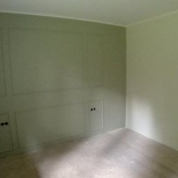 REMONTY DAMIAN DUSZCZAK - Pokój po malowaniu ścian na jasny odcień zieleni z dekoracyjnymi panelami ściennymi i ukrytymi drzwiczkami rewizyjnymi; widoczne puszki z farbą w rogu.