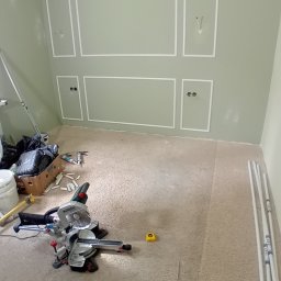 REMONTY DAMIAN DUSZCZAK - Montaż ozdobnych listew ściennych w pokoju z zielonymi ścianami, widoczna piła ukośnica, listwy przypodłogowe i narzędzia.