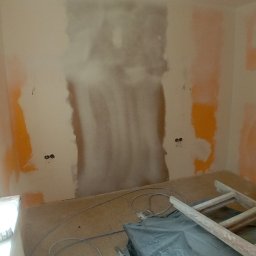 REMONTY DAMIAN DUSZCZAK - Pokój w trakcie przygotowania do malowania: częściowo zagruntowana ściana, zabezpieczone gniazdka, przewody na podłodze, drabina i folia ochronna.