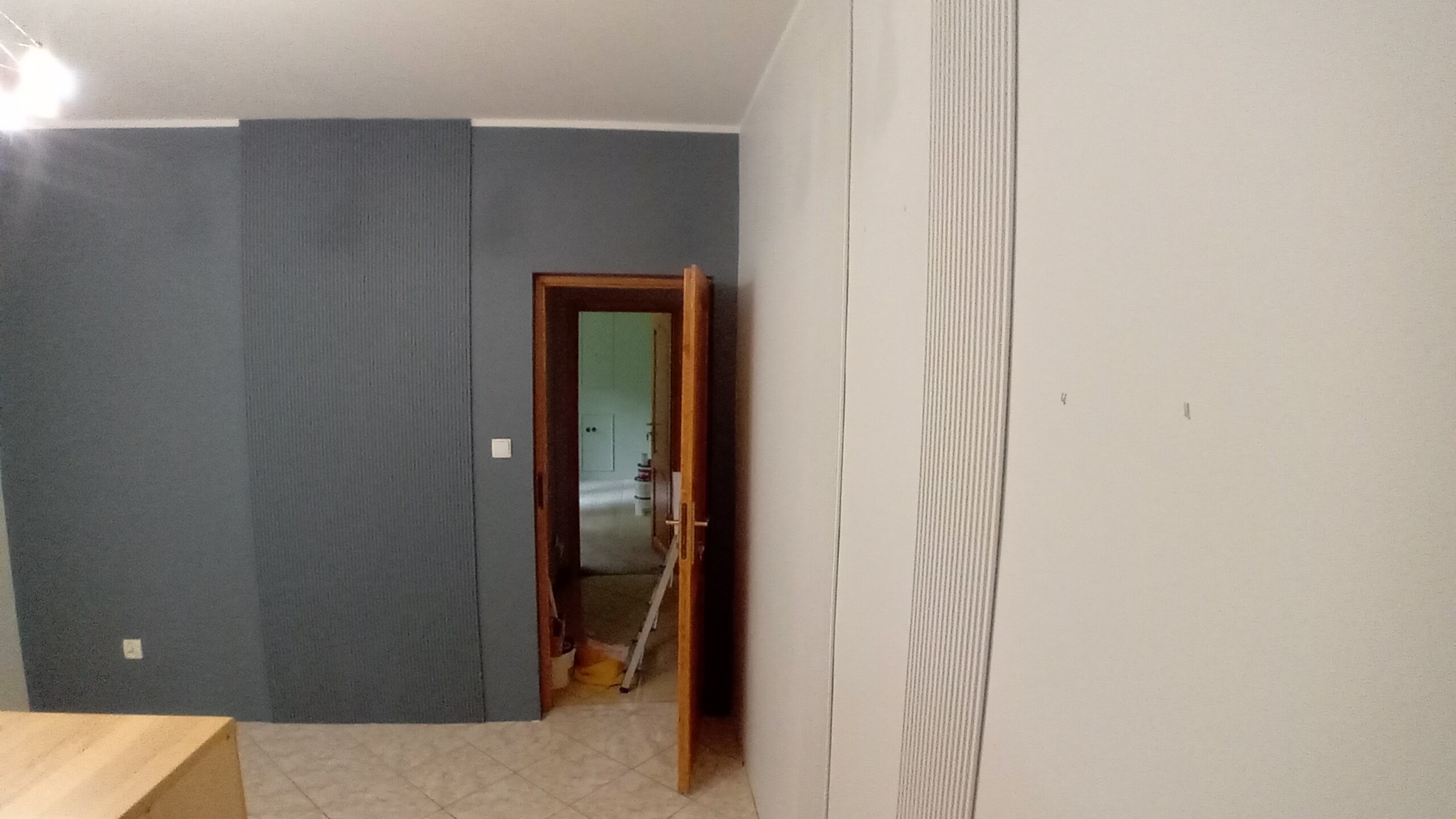 Szara ściana z dekoracyjnymi panelami w Brodnicy, widoczne otwarte drzwi z drabinką w tle i biała szafa przesuwna.