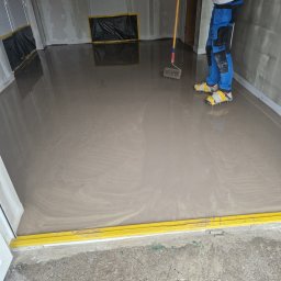 BUD-MAT - Wyrównywanie wylewki samopoziomującej wałkiem z kolcami w Poznaniu, widoczne buty z kolcami na nogach wykonawcy.