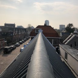 DAVLATBUD - Widok z góry na dach budynku z pracującym dekarzem; w tle zabudowa miejska i pochmurne niebo.