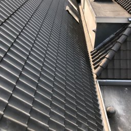 DAVLATBUD - Nowy, grafitowy dach z dachówki ceramicznej, widok z góry, z fragmentem płaskiego dachu i pracującym dekarzem w tle.