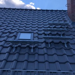 DAVLATBUD - Ciemna dachówka ceramiczna z zamontowanym oknem dachowym i metalowymi pomostami roboczymi, widok na błękitne niebo z chmurami.