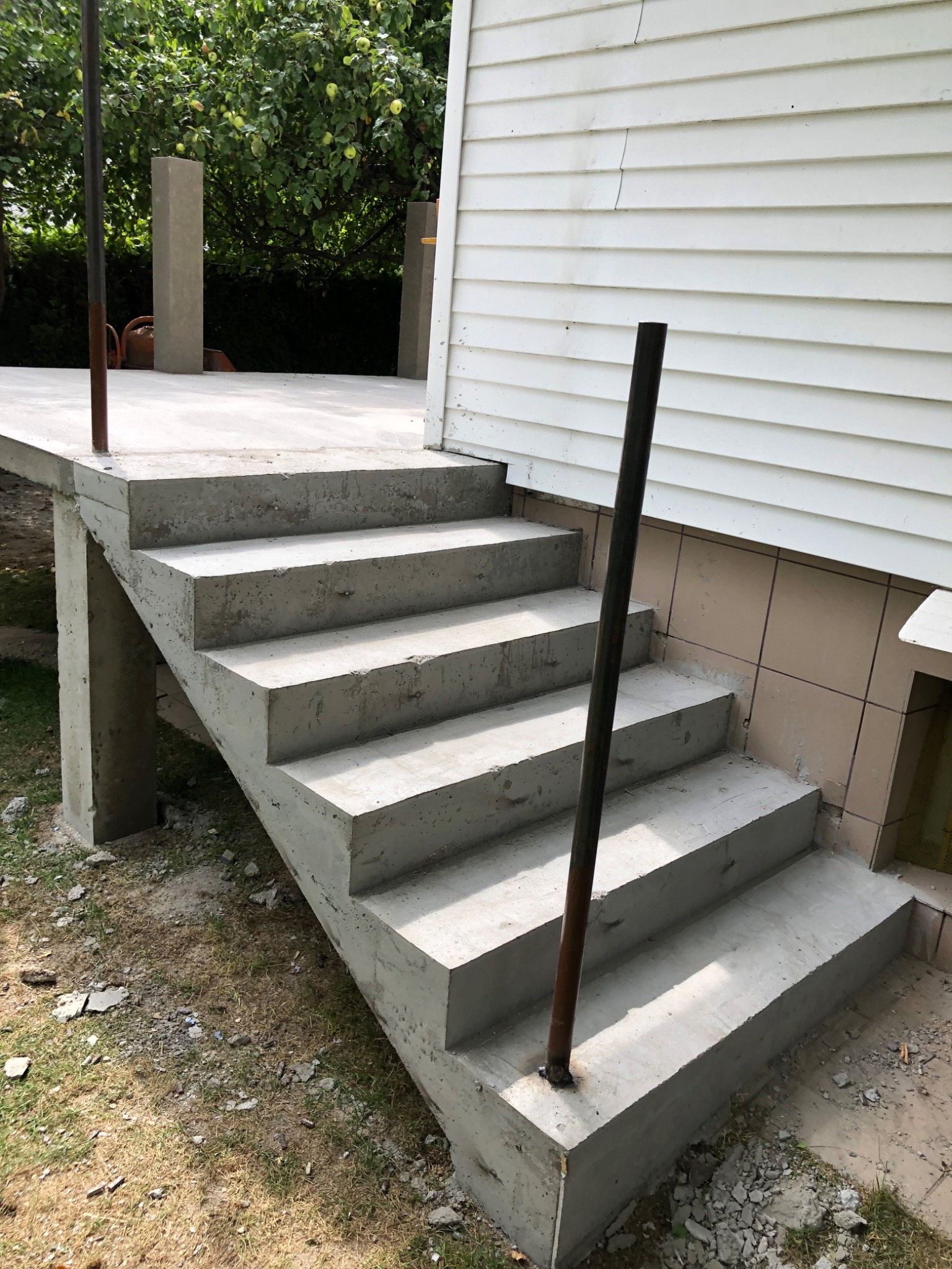 Betonowe schody wejściowe do domu z białymi panelami elewacyjnymi, widoczne przygotowane słupki na balustradę.