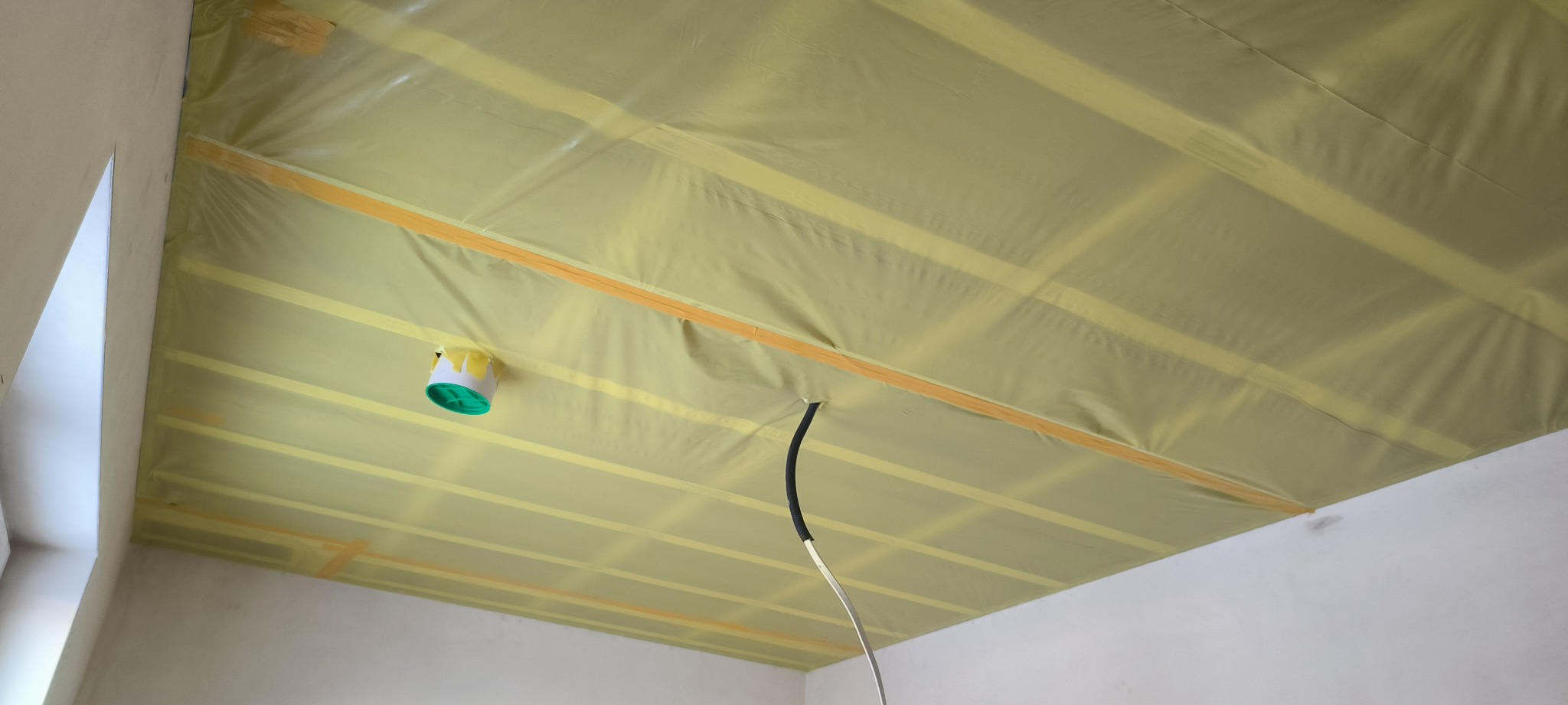 Ocieplenie poddasza wełną mineralną, zabezpieczone folią paroizolacyjną, widoczne drewniane belki konstrukcyjne i wystający kabel elektryczny.