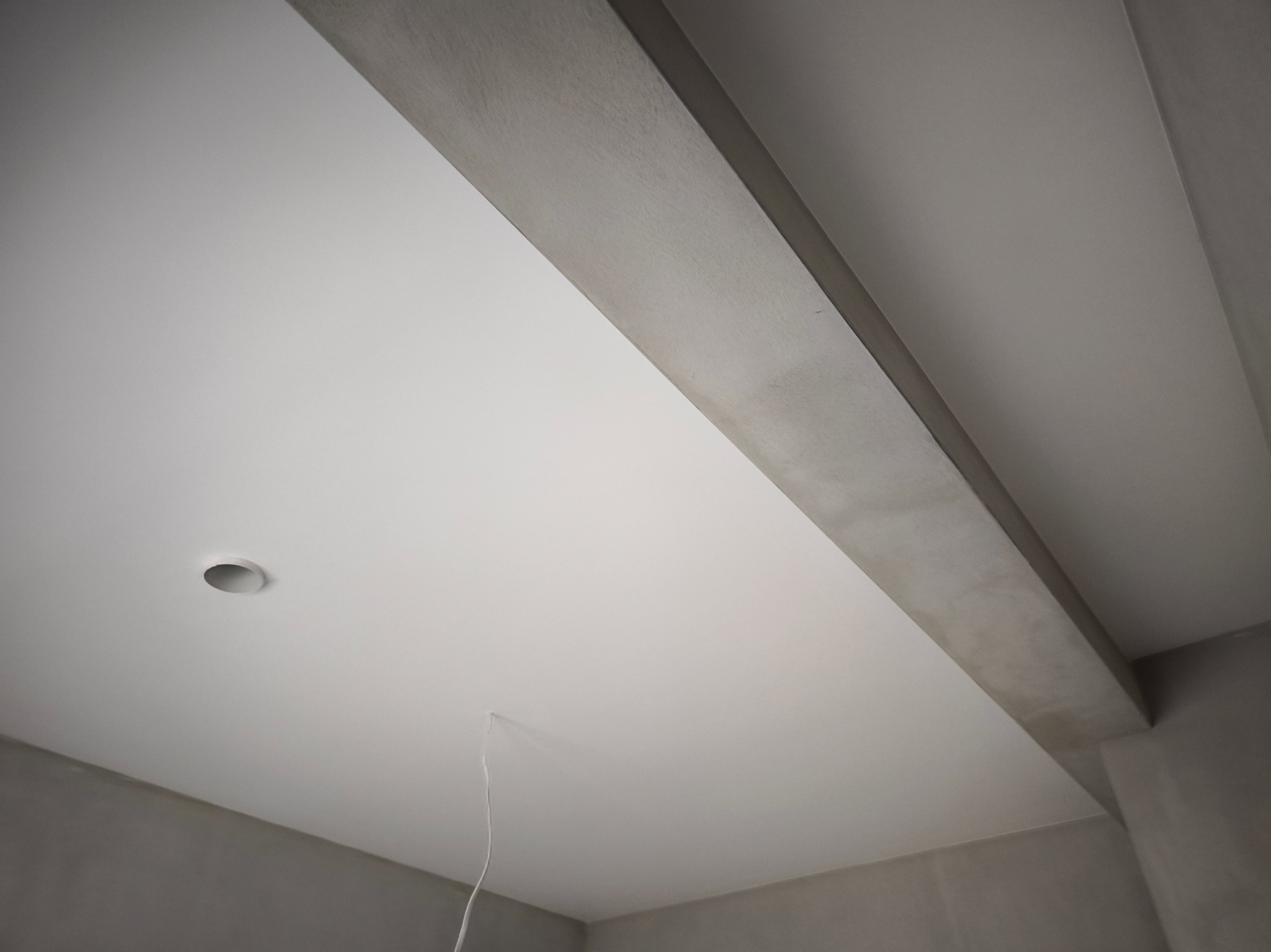 Gładki, biały sufit z zamontowanym punktowym oświetleniem i szarą belką konstrukcyjną. Widok z dołu, podkreślający precyzję wykończenia.