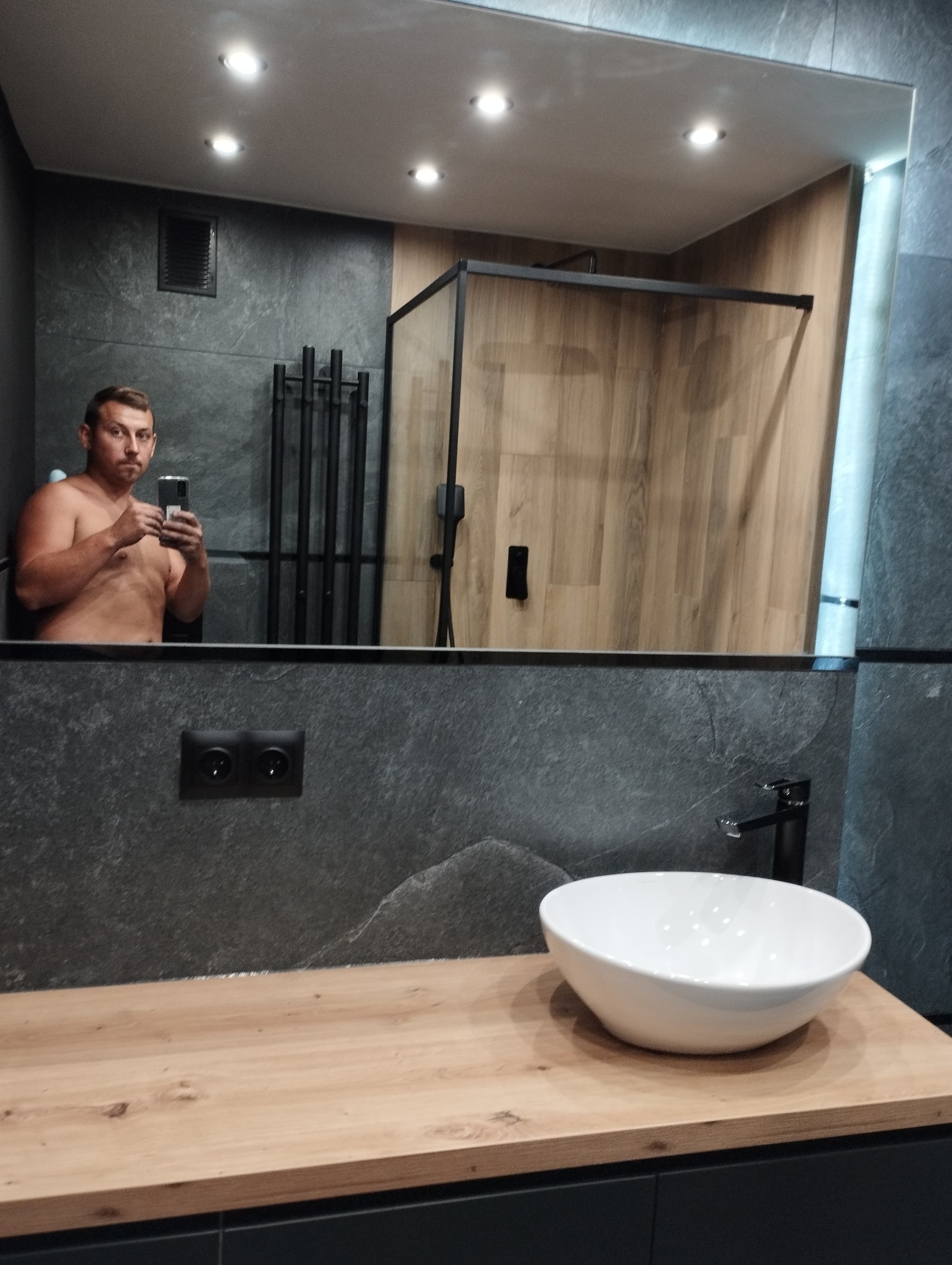 Nowoczesna łazienka z umywalką nablatową i kabiną prysznicową typu walk-in, widoczna w lustrze osoba robiąca zdjęcie.